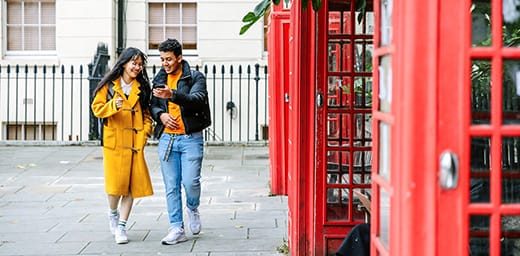 Two people wearing yellow walking next to red phone boxes