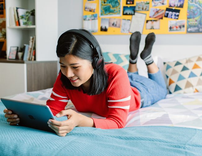 Student laying on bed in her student accommodation studying