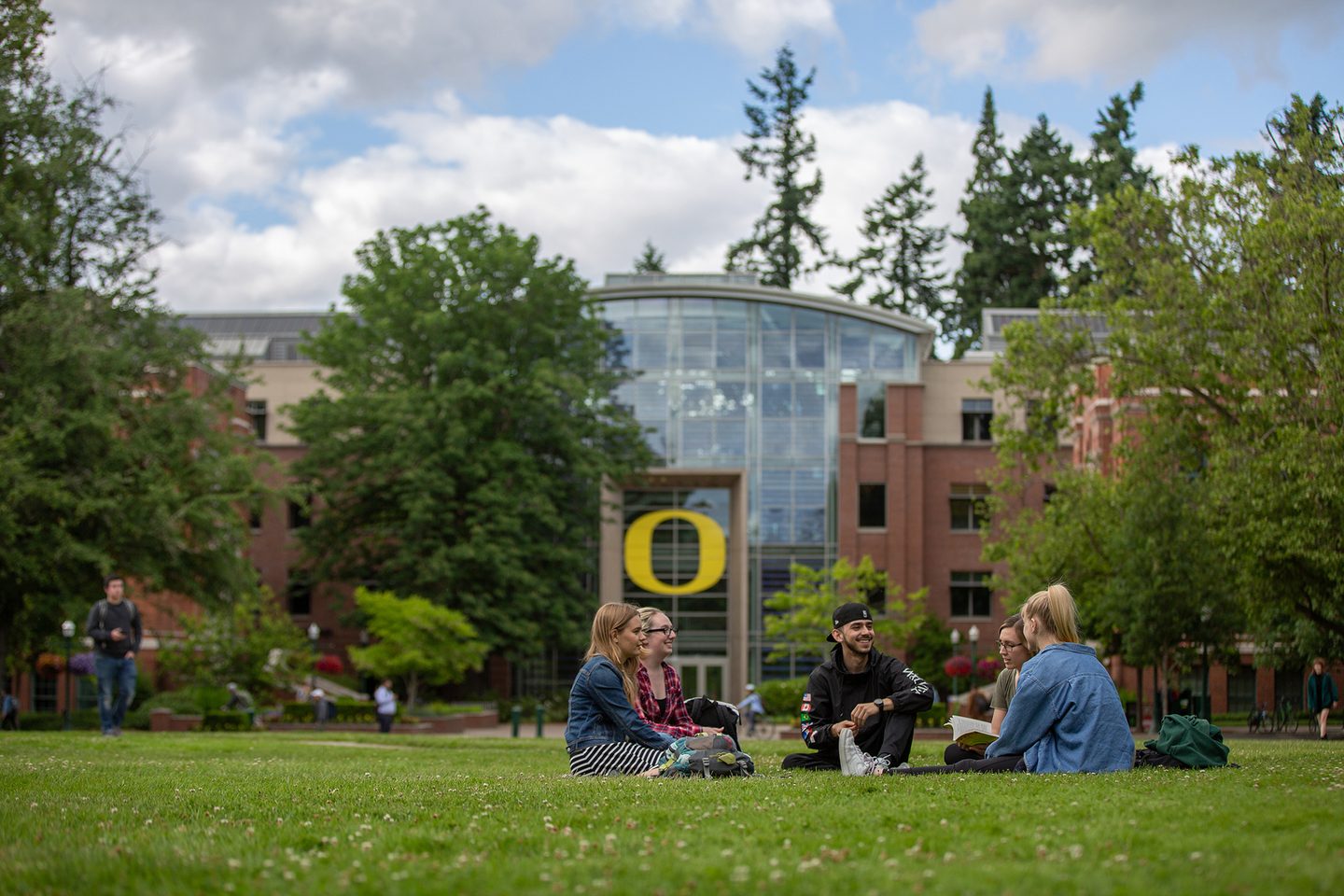 Five students sitting down on the campus green park socialising