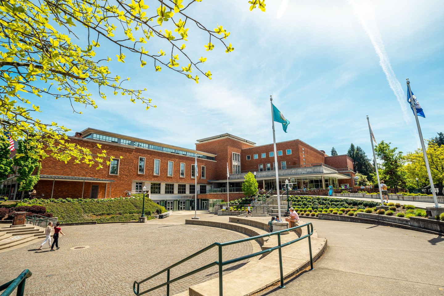 Clear skies and bright sun day while students walk in front of a campus building