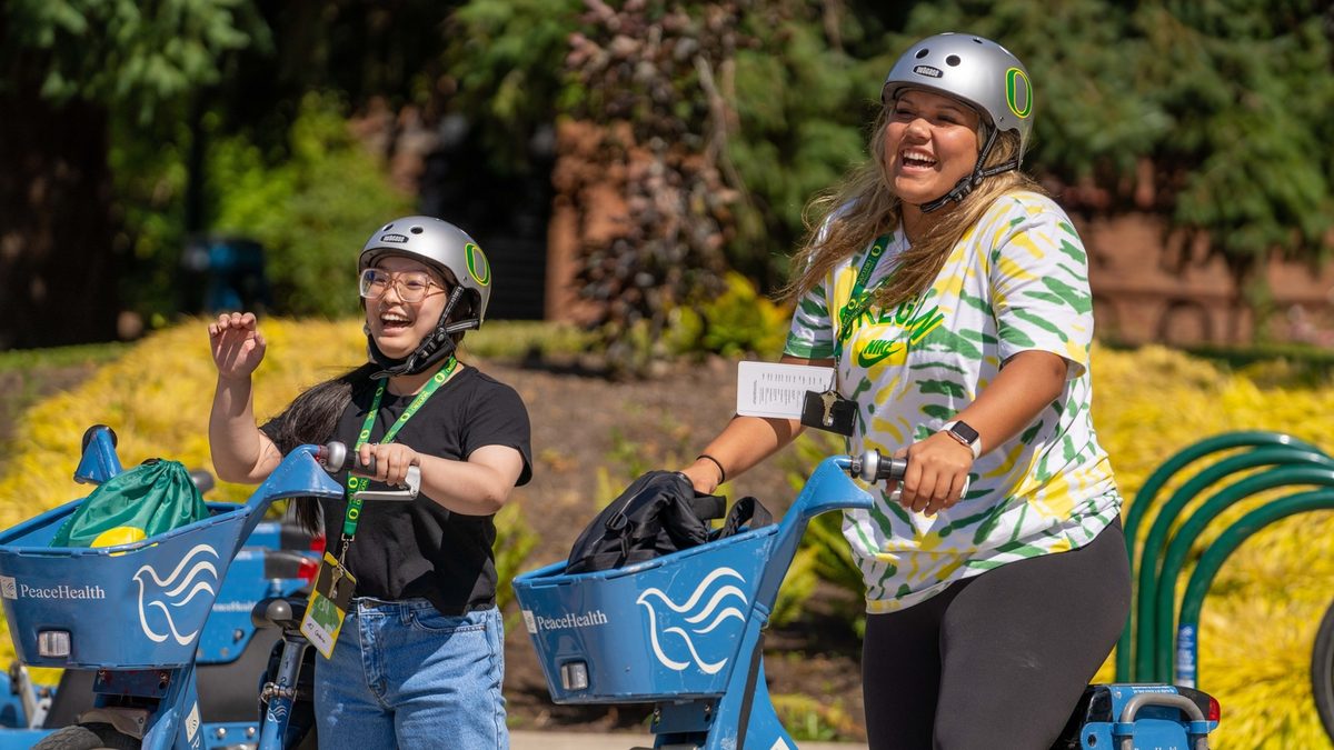 Two smiling students on their campus public bikes