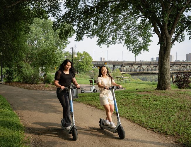 Two students traveling through campus on E-Scooters